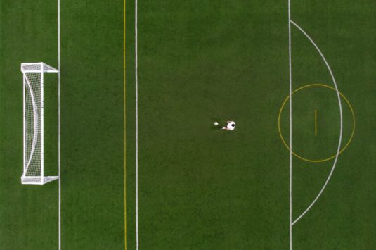 Overhead view of soccer field with player standing in front of the penalty box.
