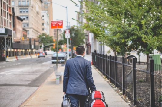 A man in a suit walking down a city street with luggage representing resignation from a job