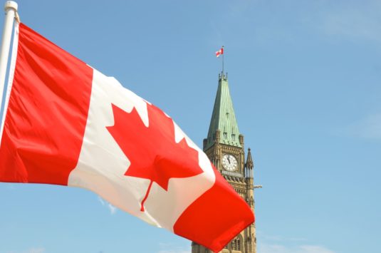 The Canadian flag waving in front of the Parliament building tower