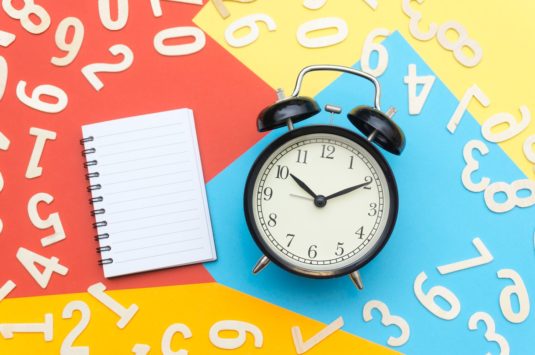 An alarm clock surrounded by numbers and a notebook representing new tax deadlines in Canada