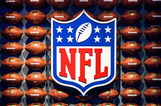 The NFL logo against a backdrop of footballs representing NFL fallout from COVID-19