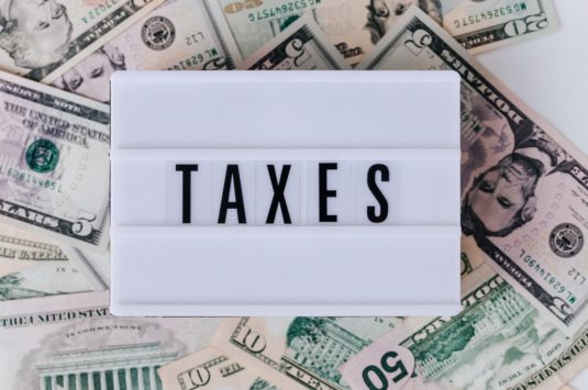 A sign that says taxes on a pile of US money representing the tax benefits of renouncing citizenship