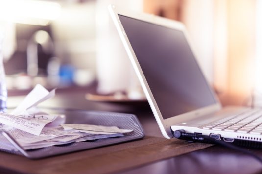 A laptop next to a tray of receipt representing a tax scam involving inflated charitable donation receipts